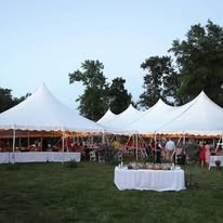 Row of white pole tents with guests and a buffet table at an evening reception