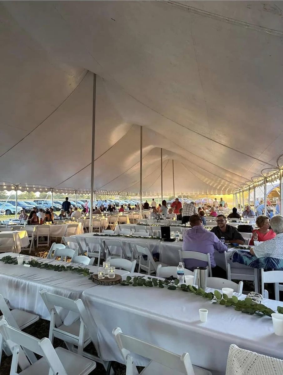 Guests seated at long tables with white linens under a pole tent